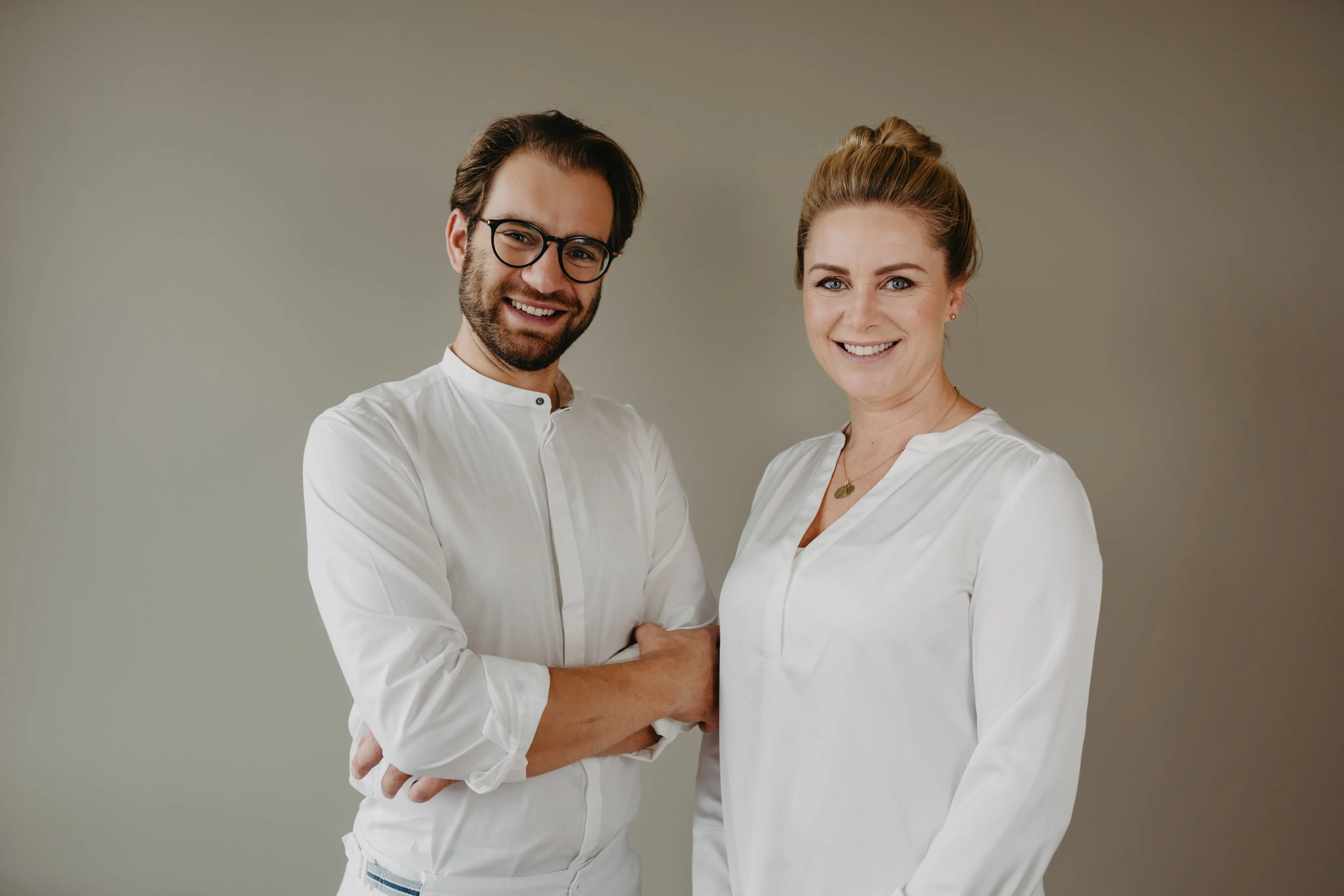 Bünger & Meißner – Ein Mann mit Brille und eine Frau im weißen Hemd lächeln in die Kamera