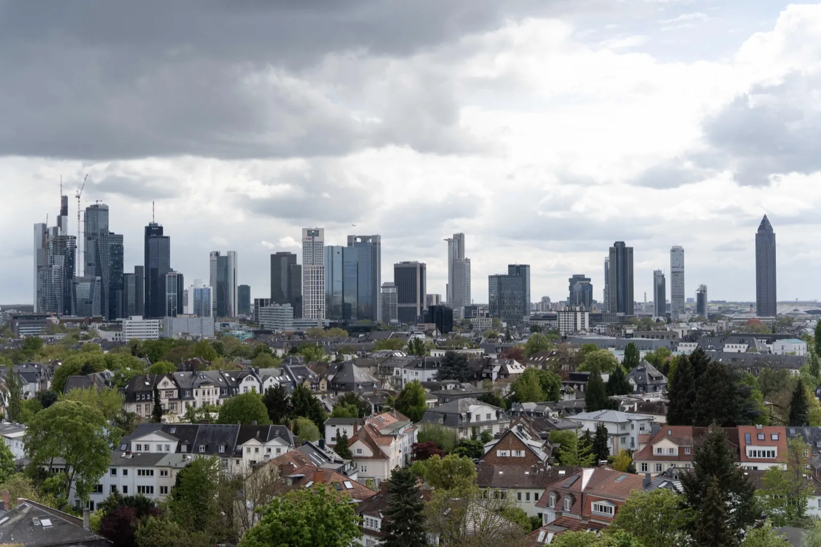 Frankfurt School – Eine Weitwinkelaufnahme der Frankfurter Skyline mit Wohngebäuden im Vordergrund unter bewölktem Himmel