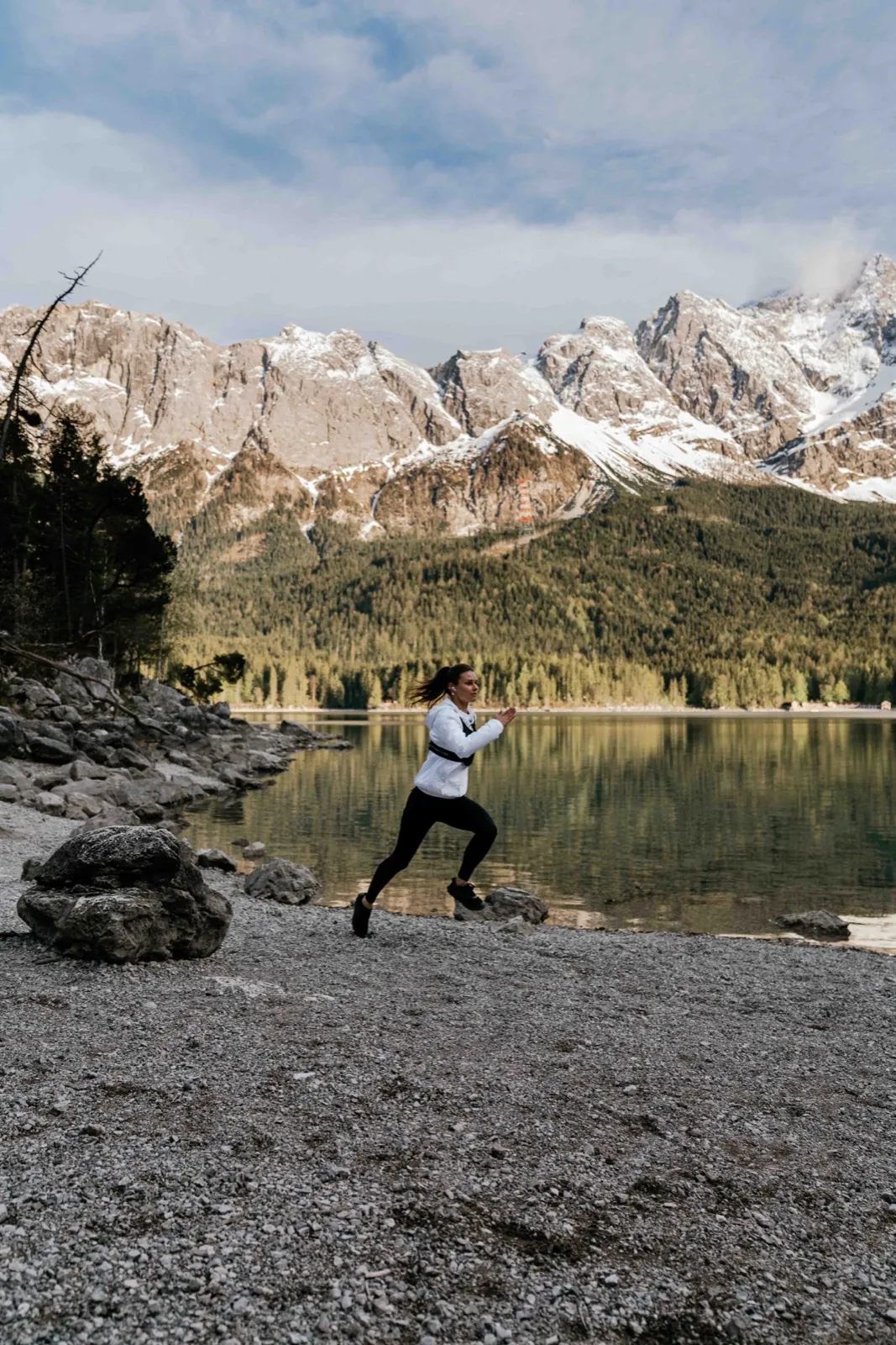 Freetrain – Eine Frau joggt am Ufer eines Bergsees vor einer schneebedeckten Bergkulisse