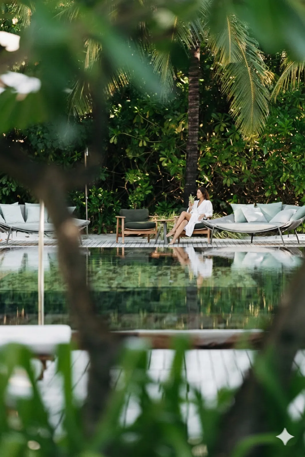 Patina Maldives – Eine Frau im weißen Bademantel entspannt auf einer Liege am Pool eines tropischen Resorts