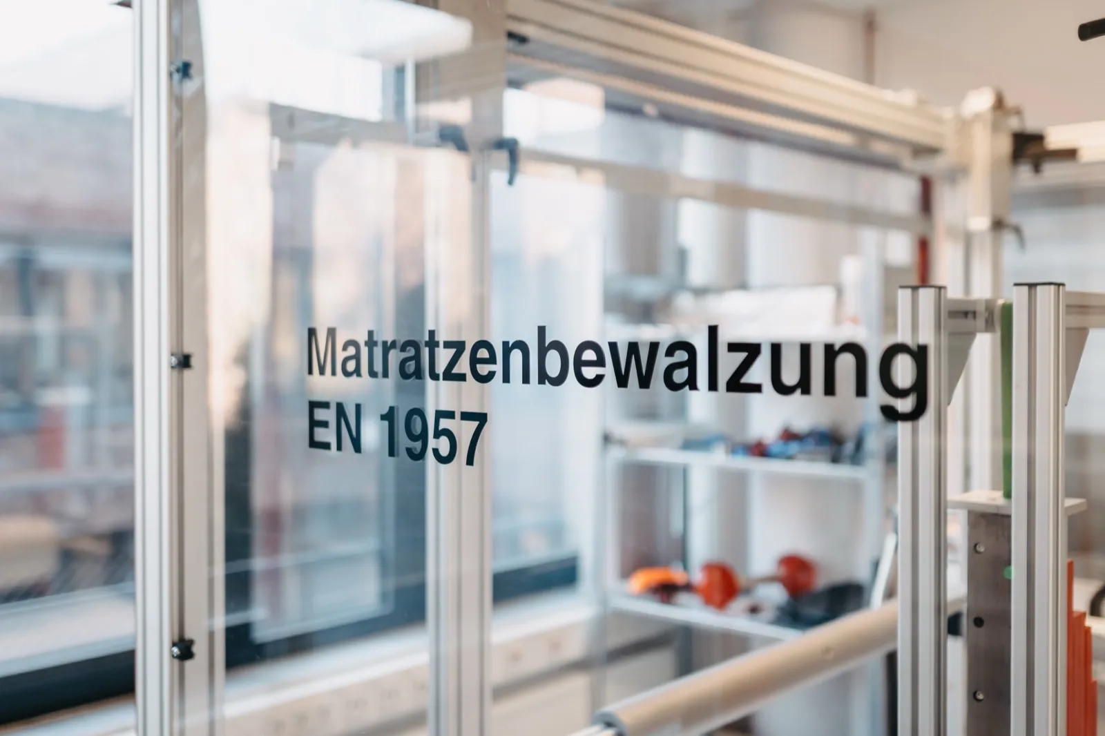 QIMA – Eine Glasscheibe mit der Aufschrift 'Matratzenbewalzung EN 1957' in einem Prüflabor
