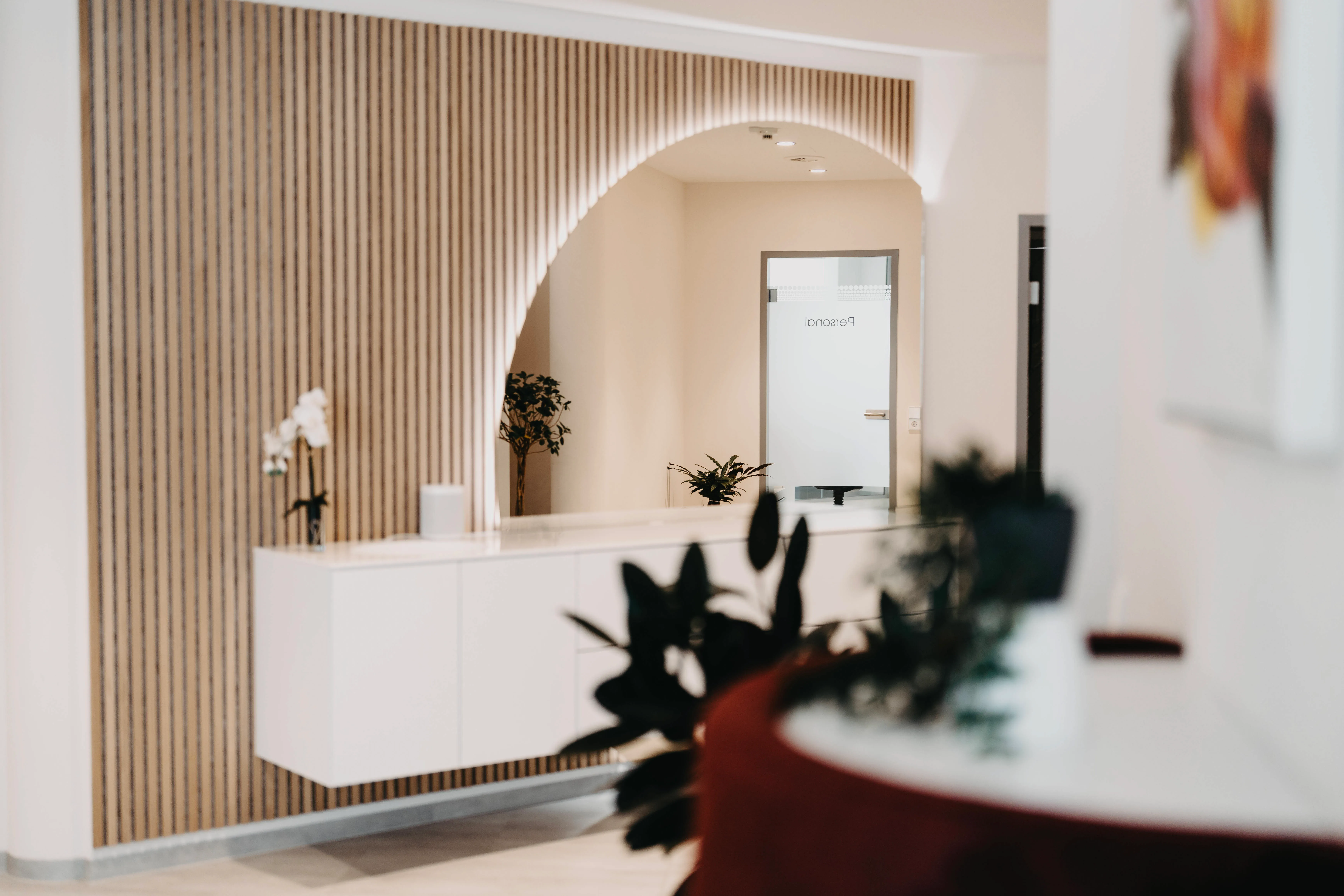 ZahnZentrum 79 – Ein moderner Empfangsbereich mit einer Holzlamellenwand und einem großen, beleuchteten Bogenspiegel